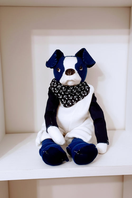 Stuffed toy dog with blue outfit and black and white scarf on a beige surface
